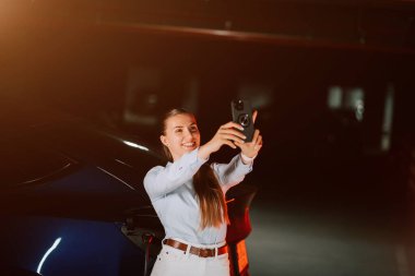 Kadın akşam saatlerinde şehir merkezinde neon ışıkların keyfini çıkarırken elektrikli araba yüklüyor.