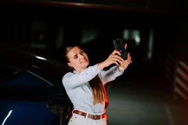 Kadın geceleri şehir otoparkındaki neon ışıklarının altında elektrikli araba yüklüyor.