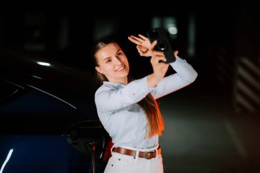 Kadın gece canlı neon ışıklarda anı yakalarken elektrikli arabayı şarj ediyor.