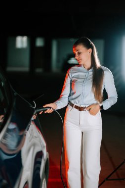 Parlak neon ışıklı bir yerde gece kadın elektrikli araba yüklüyor.