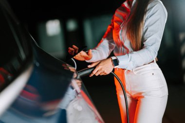 Kadın modern şarj istasyonunda neon ışıkları altında elektrikli araba şarj ediyor.