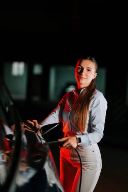 Kadın şehir merkezinde geceleri neon ışıkla elektrikli araba yüklüyor.