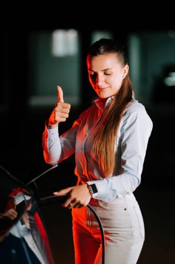 Gece park yerinde neon ışıklarının altında elektrikli araba yükleyen bir kadın.