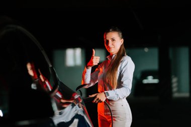 Kadın, akşam saatlerinde neon ışıklı otoparkta elektrikli araba şarj ediyor.