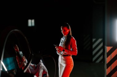 İş kadını akşam saatlerinde yeraltı otoparkında elektrikli araç şarj ediyor.