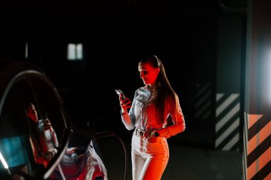 İş kadını cep telefonu kullanırken yeraltı otoparkında elektrikli araba şarj ediyor.