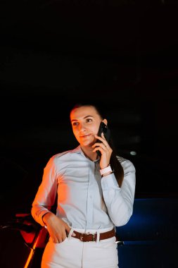 İş kadını, yeraltı otoparkında telefonla konuşurken elektrikli araçtan para alıyor.