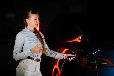 İş kadını cep telefonu kullanırken yeraltı otoparkında elektrikli aracı şarj ediyor.