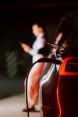 İş kadını telefonunu kullanırken elektrikli aracı yeraltı otoparkında şarj ediyor.
