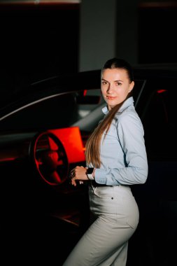 Akşam saatlerinde loş bir ortamda şık bir kadın arabanın yanında poz veriyor.