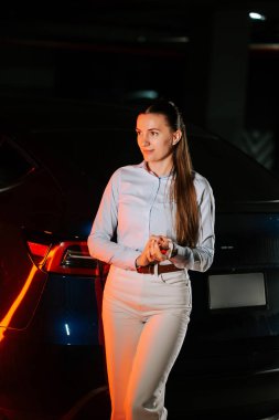 Gece bir otoparkta bir arabanın yanında duran kadın.