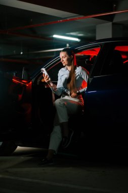 Genç bir kadın gece otoparkta telefonunu kontrol ederken arabada dinleniyor.