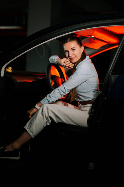 Уверенная женщина, сидящая в машине с ярким внутренним освещением ночью