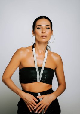 Model, stüdyo ortamında siyah kıyafetler ve parlak aksesuarlarla poz veriyor.