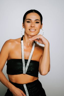 Zarif bir kadın şık siyah kıyafetler içinde ışıltılı detaylar ve kendine güvenen bir gülümsemeyle poz verir.