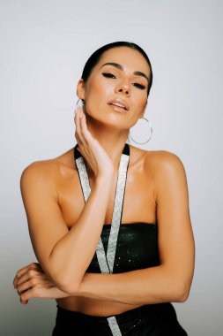 Model, bir stüdyo ortamında şık kıyafetler ve cesur aksesuarlarla güven içinde poz verir.