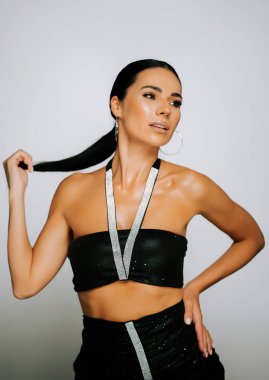 Model, bir stüdyo ortamında parıldayan detaylarla şık bir siyah elbise sergiliyor.