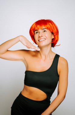 Parlak turuncu saçlı neşeli genç bir kadın şık siyah bir elbise içinde oyuncu bir çekim için poz veriyor.