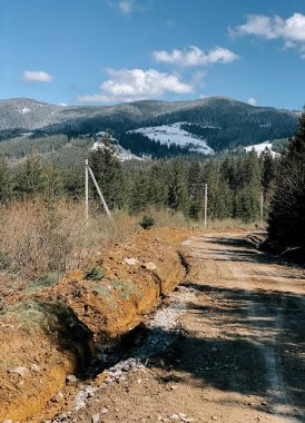 Baharın güneşli bir gününde ağaçlar ve tepelerle çevrili dağ yolu.