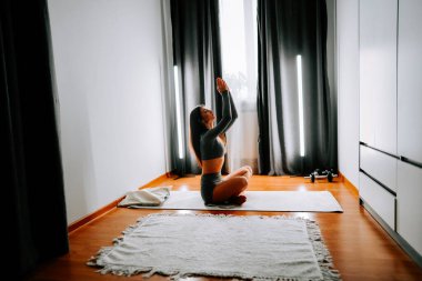 Genç bir kadın sabahları huzurlu ve aydınlık bir odada yoga yapıyor.