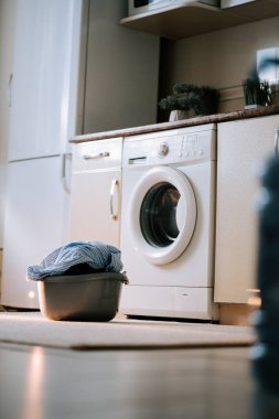 Güneşli bir günde çamaşır makinesi ve sepetle modern bir çamaşırhanede kirli çamaşırları yıkamak.