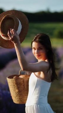 Güneşli bir günde lavanta tarlalarında hasır şapka takan ve sepet taşıyan bir kadın.