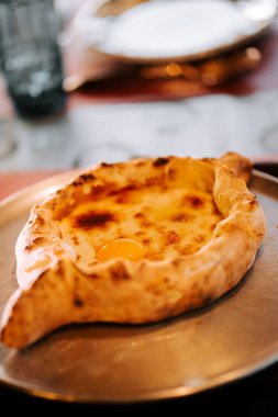 Geleneksel Adjarian Khachapuri 'nin tadını çıkarırken zengin peynir ve yumurtayla metal bir tabakta taze servis edildi.