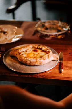 Lezzetli Adjarian Khachapuri sıcak bir yemek ortamında metalik bir tabakta servis edilir.