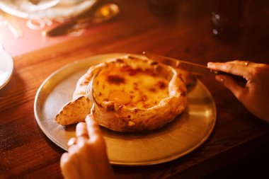 Konforlu bir restoranda peynir ve yumurtalı geleneksel Adjarian Khachapuri 'nin tadını çıkarıyorum.