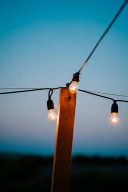 Açık hava sicim ışıkları, alacakaranlıkta yumuşak mavi tonlarıyla sakin bir akşam gökyüzünü aydınlatır.