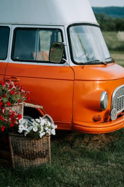 Kırsal kesimde güneşli bir öğleden sonra çiçek sepetlerinin yanına park edilmiş turuncu bir minibüs.