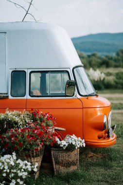 Parlak turuncu yemek kamyonu çiçeklerin arasına park etmiş kırsal bir alanda.