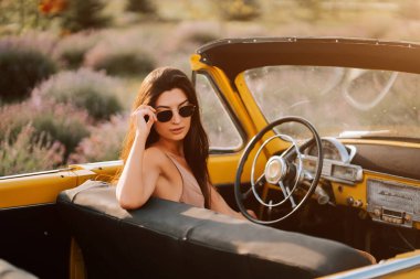 Genç bir kadın, bir tarlaya park edilmiş üstü açık bir arabada yaz gününün tadını çıkarıyor.