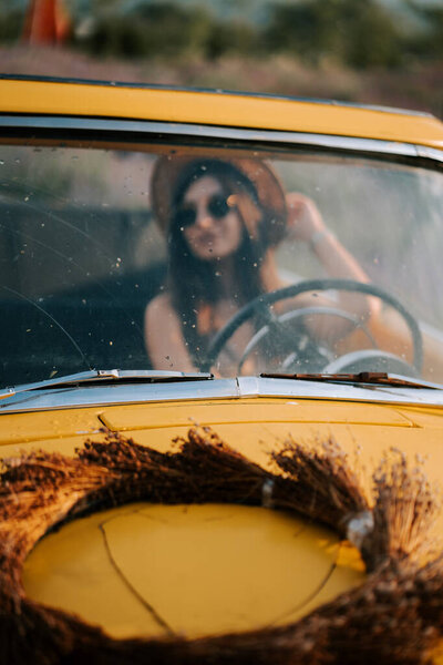 Woman driving a vintage yellow car during a sunny day in the countryside