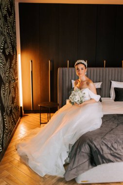 Gelin, düğünden önce modern otel odasında yatağında oturuyor.