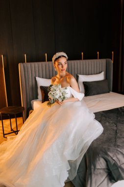 Düğün töreninden önce modern otel odasında yatağında oturan zarif gelin.