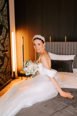 Gelin, düğün töreninden önce lüks modern otel odasında buketle zarif poz veriyor.