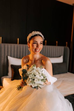 Seremoniden önce şık bir otel odasında elinde buket tutarken gülümseyen güzel gelin.