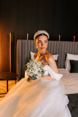 Modern bir otel odasında zarif dekorlu ve hafif ışıklandırmalı bir gelin portresi.