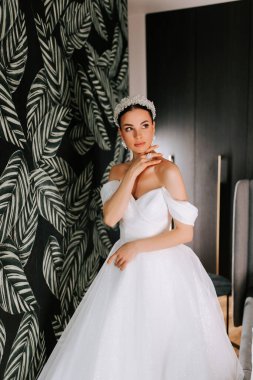 Zarif gelin, tropik yaprak duvar kağıdına karşı çarpıcı beyaz elbiseyle poz veriyor.