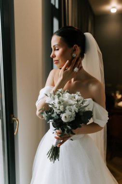 Gelin doğal ışıkla zarif bir mekanda düğün hazırlığı yapıyor.