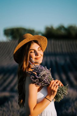 Genç bir kadın gün batımında elinde taze lavanta buketi tutarken lavanta tarlalarını seviyor.