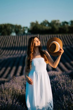 Beyaz elbiseli kadın yaz güneşinin altın saatinde lavanta tarlasından zevk alıyor.