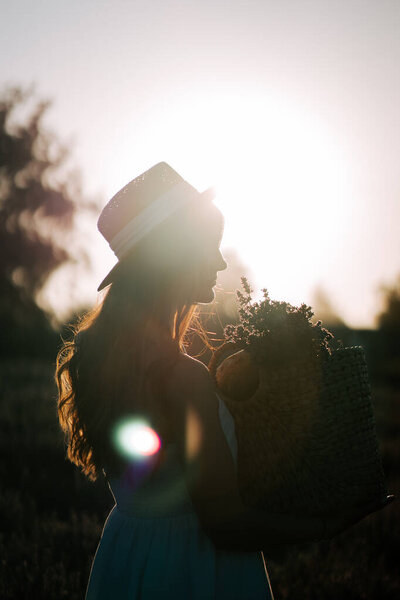 Woman in silhouette holding a basket of flowers during sunset in a rural setting