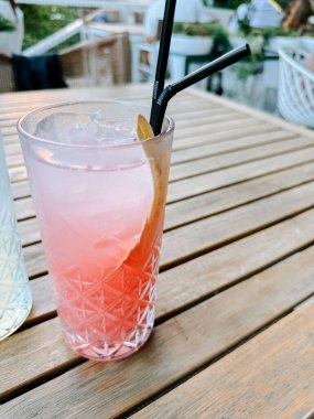 Güneşli bir mekanda, ahşap bir masada uzun bir bardakta servis edilen ferahlatıcı kokteyl.