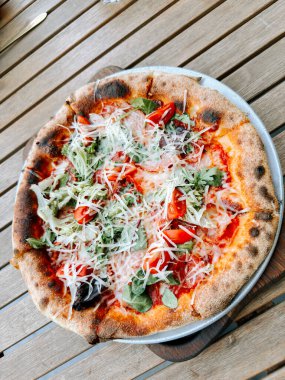 Sıcak bir ortamda ahşap bir masada servis edilen taze sebzeli pizza.