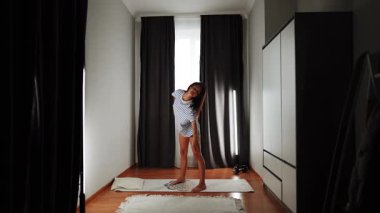 Genç bir kadın sabah vakti şık bir odada yoga yapıyor.