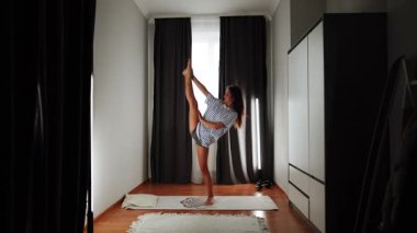 Evde yüksek tekme ile yoga alıştırması ve dingin bir ortamda denge ve esneklik üzerinde odaklanmak