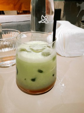 Kafe ortamında, yemek masasında buzlu bir bardakta servis edilen yeşil çay.