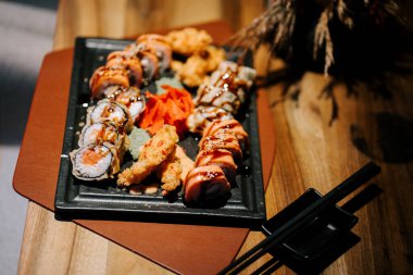 Restoranda siyah tepside servis edilen çeşitli rulo ve karidesli suşi tabağı.